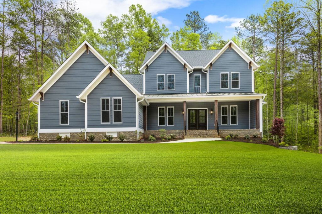 The McIlroy, a blue two-story home with stone accents and a front porch on a wooded lot